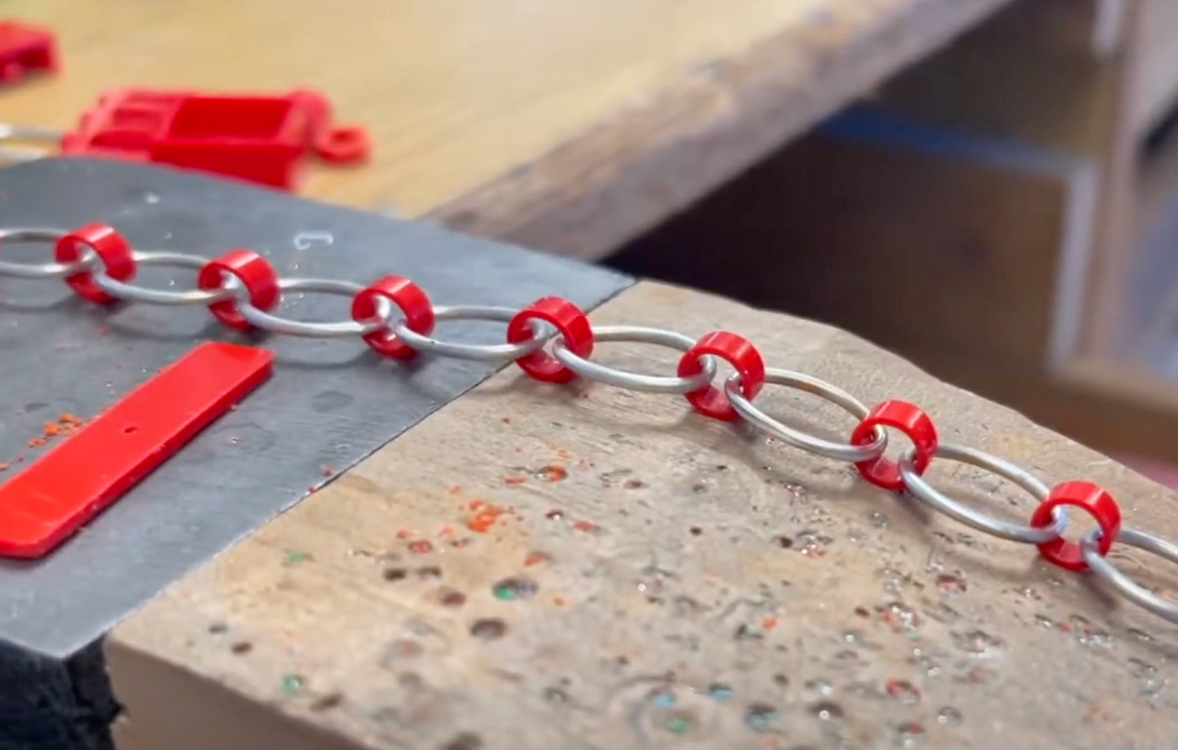 On the work bench is sterling silver links connected with red recycled lego bricks