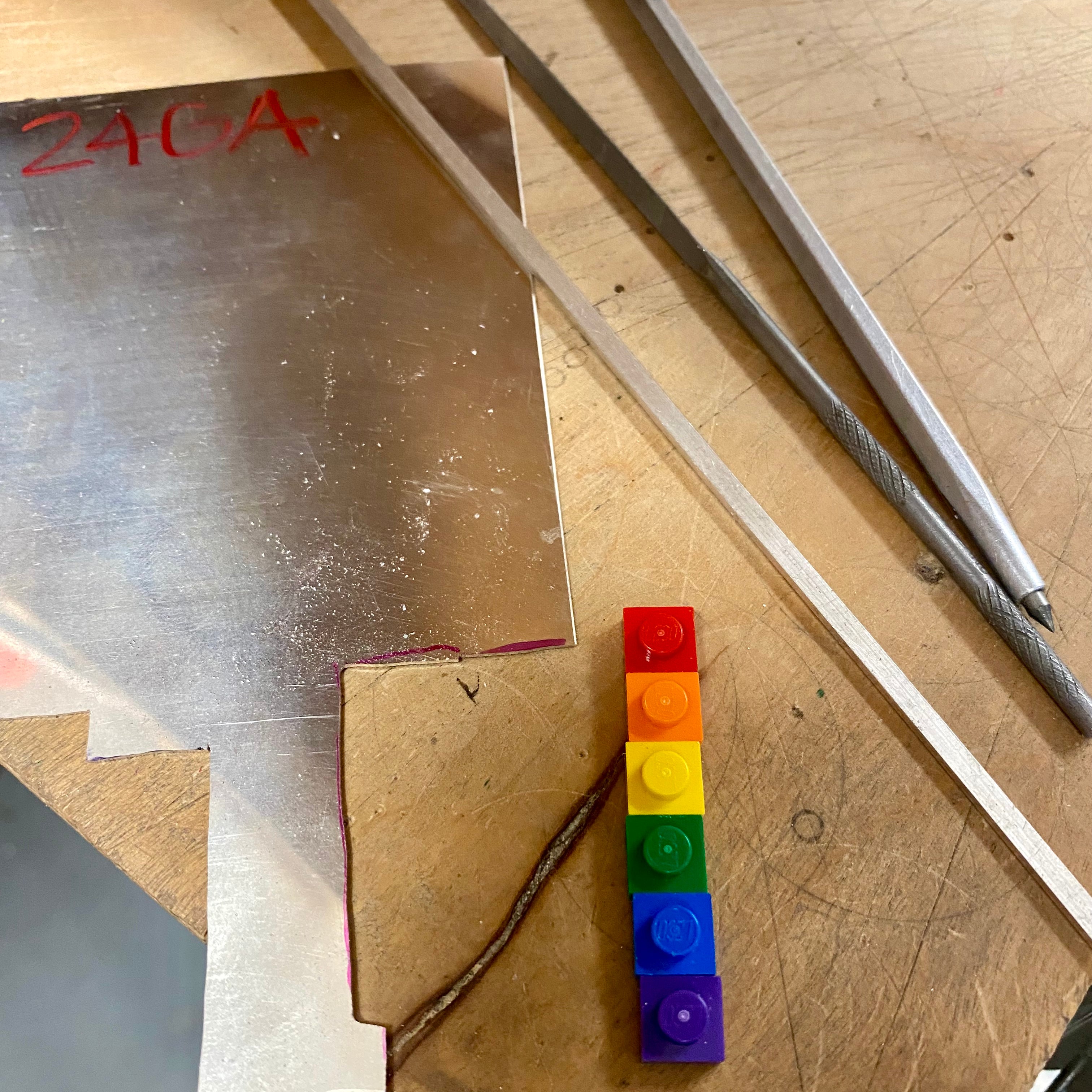 on the work bench with a piece of sheet silver, 6 lego bricks -the color of the rainbow, jewelers files and a diamond scribe