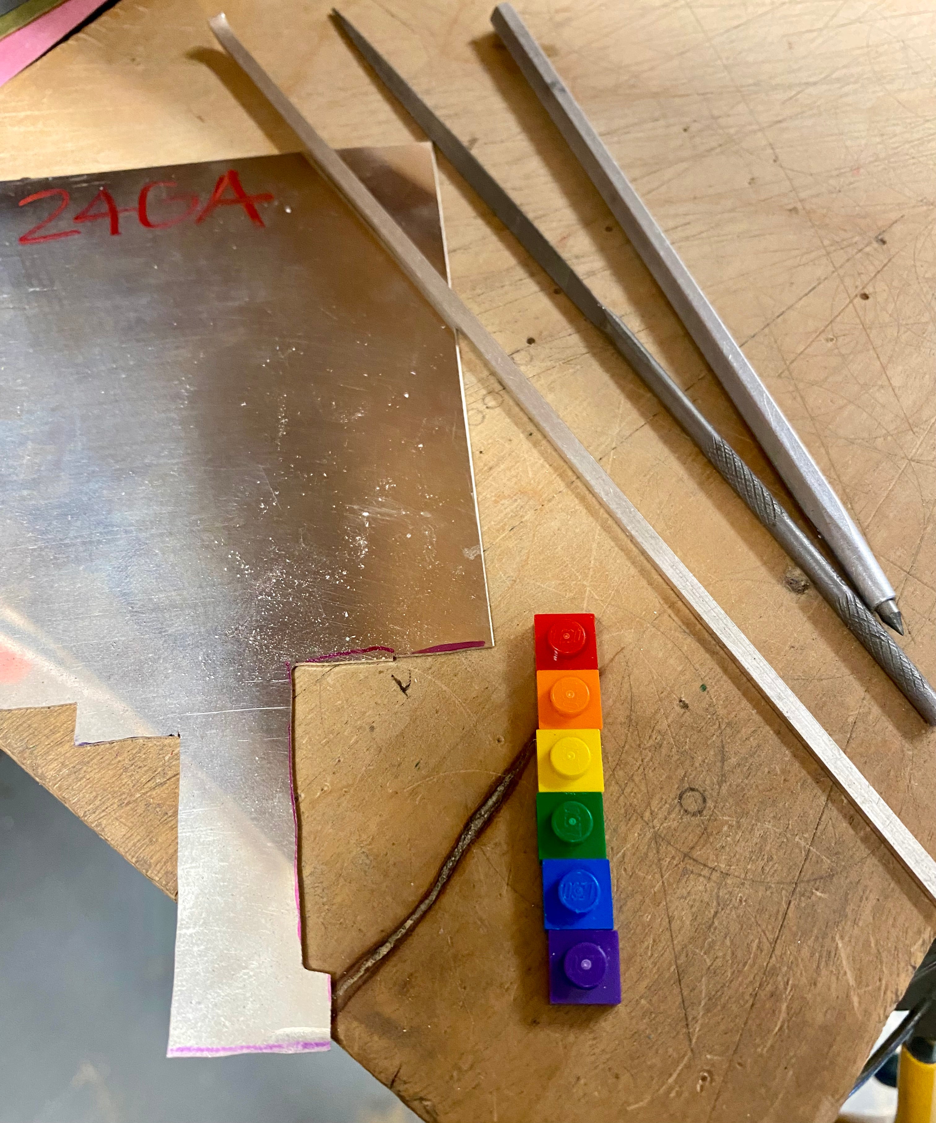 on the work bench with a piece of sheet silver, 6 lego bricks -the color of the rainbow, jewelers files and a diamond scribe