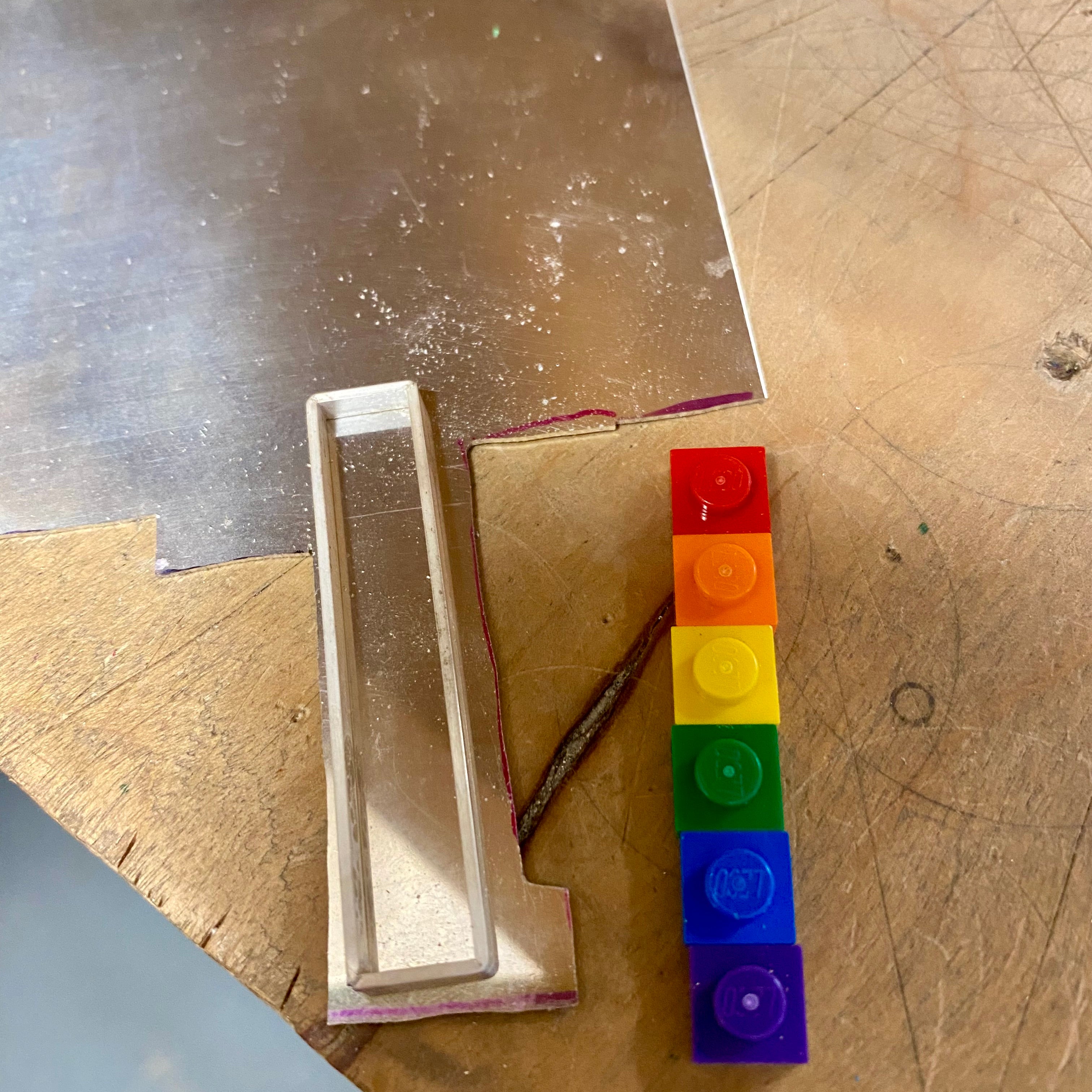 on the work bench showing the process of how the pendant is created with first shaping the bezel that will surround the lego pieces