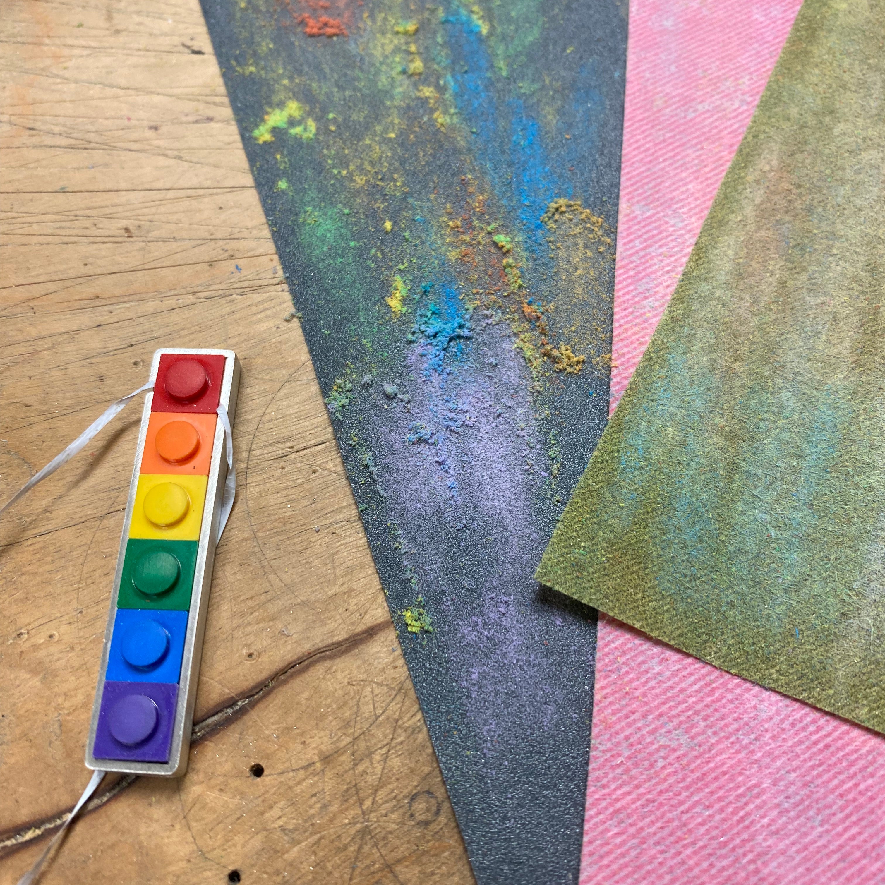 On the work bench showing the step of how the lego pieces are tested to fit tightly by putting them inside the bezel using dental floss underneath so they can be taken out with a pull on the dental floss. Sandpaper is shown in different grids with lego dust on them to show how the lego are sanded