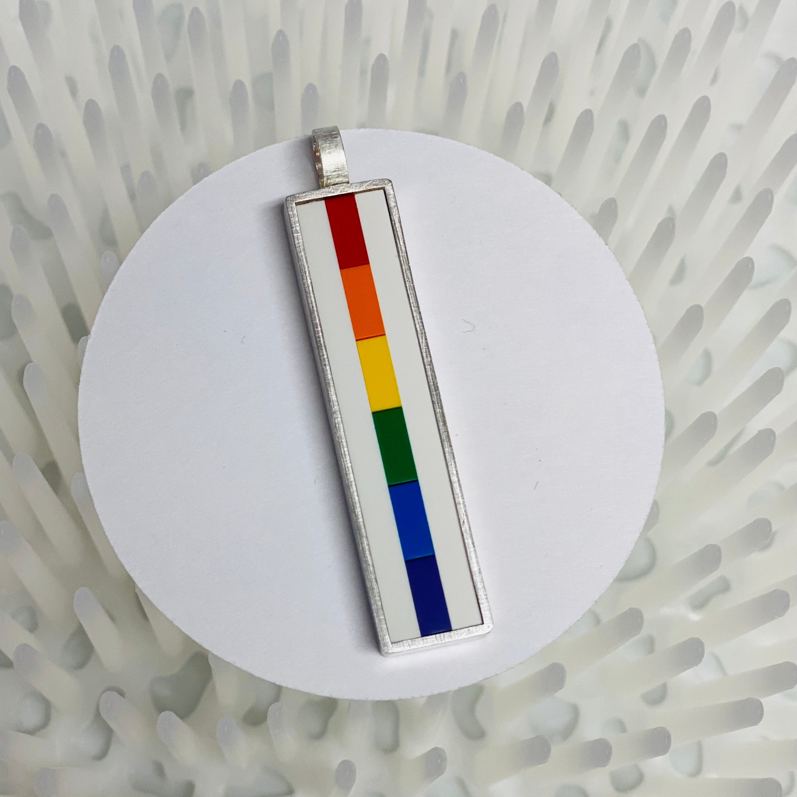Rainbow Lego pendant made with each color of the rainbow in lego bricks going down vertically  being displayed on a white circle