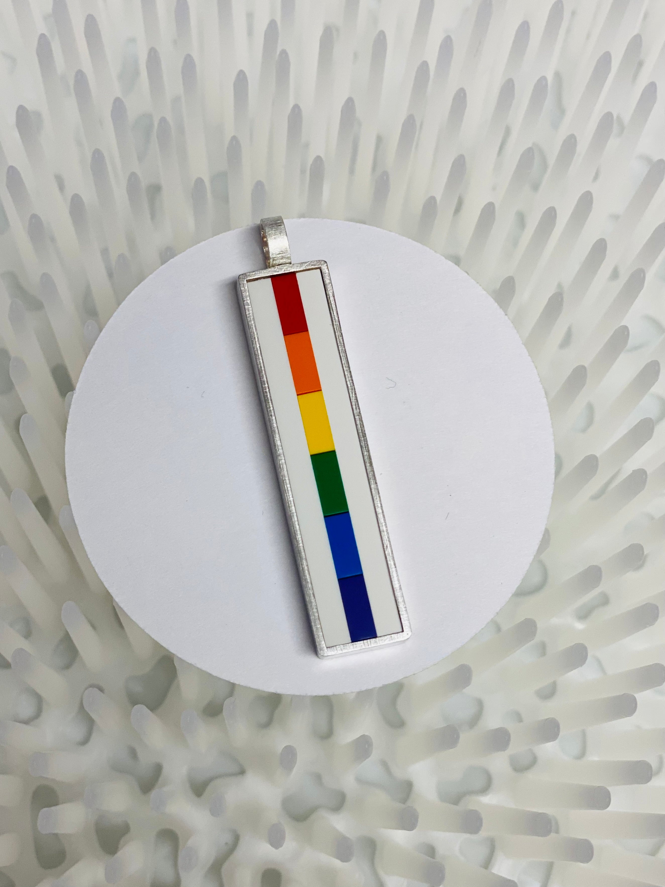 Rainbow Lego pendant made with each color of the rainbow in lego bricks going down vertically  being displayed on a white circle