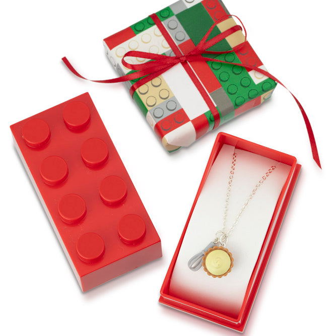 Red Lego gift box wrapped in Lego pattern paper with red bow, displayed with a Lego charm necklace inside.