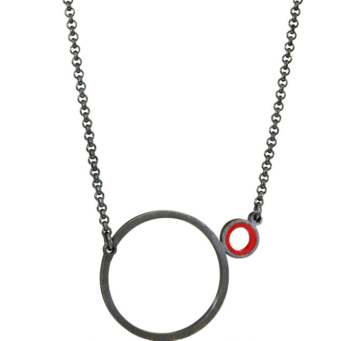 a necklace with a dark finish on the metal with a large circle pedant in center with a small circle attached to the side with a red recycled piece of a lego tube inside the small circle
