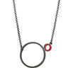a necklace with a dark finish on the metal with a large circle pedant in center with a small circle attached to the side with a red recycled piece of a lego tube inside the small circle
