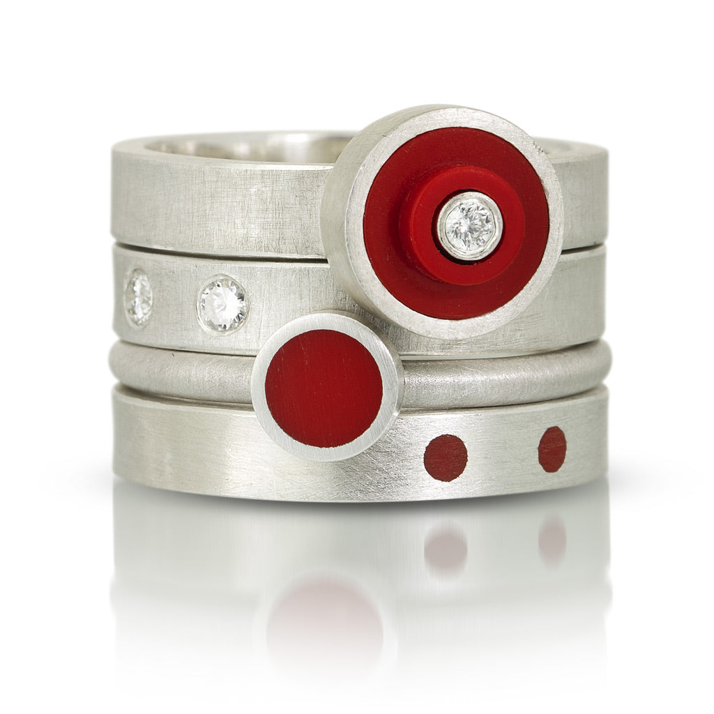 4 lego rings stacked on top of each other. First one is a round red lego dot ring with a diamond in center. Udernated that one is a band with 2 diamonds set flush into ring. Next stacking ring is a recycled red lego circle stud piece set in silver. last one on the bottom is a silve band with 2 red dots on a silver band