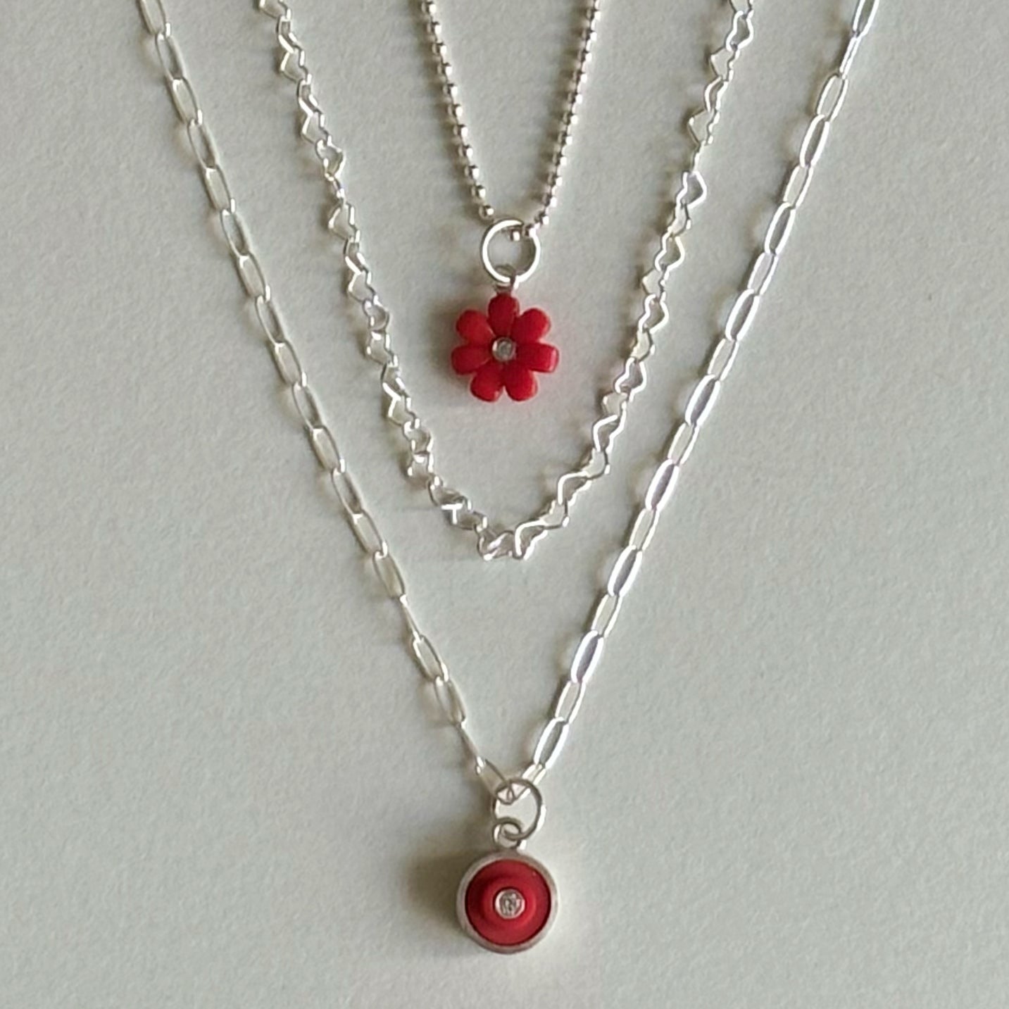 3 chains shown hanging  as if they were around a neck at different lengths with two having red lego charms to show how they can be layered stylishly.