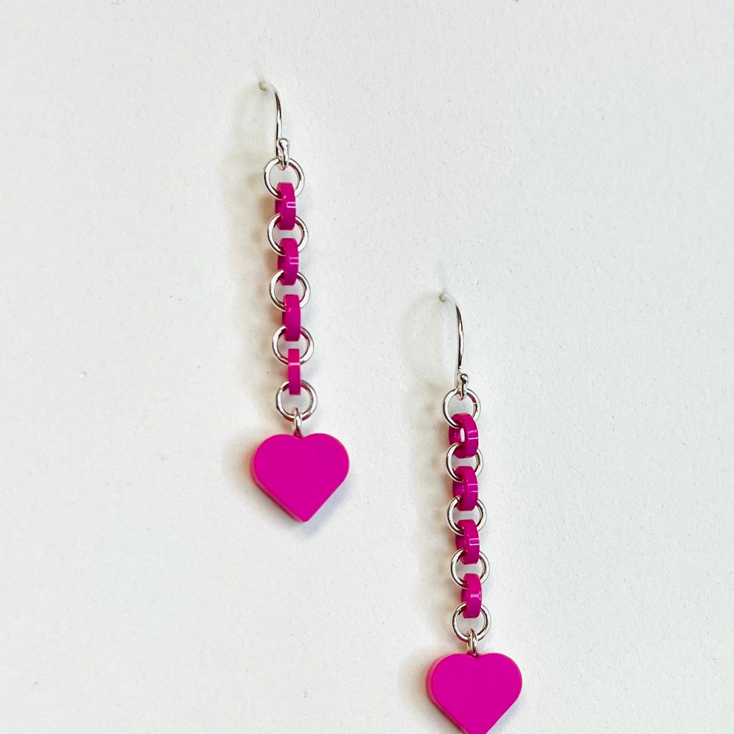 Hot pink earrings have silver jump rings alternating with loops made  from cutting off the top studs of pieces of LEGO bricks. LEGO dot heart dangles from the bottom