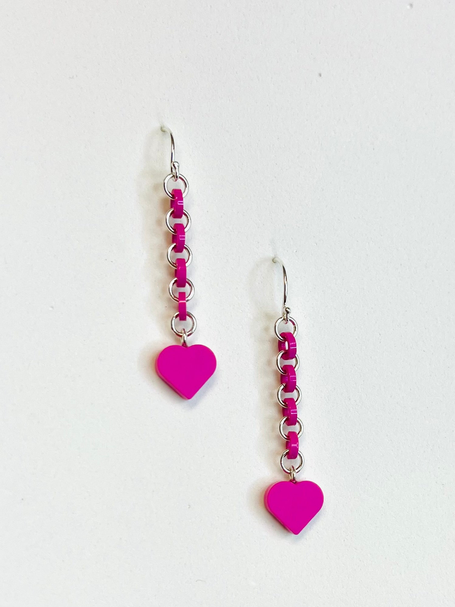 Hot pink earrings have silver jump rings alternating with loops made  from cutting off the top studs of pieces of LEGO bricks. LEGO dot heart dangles from the bottom