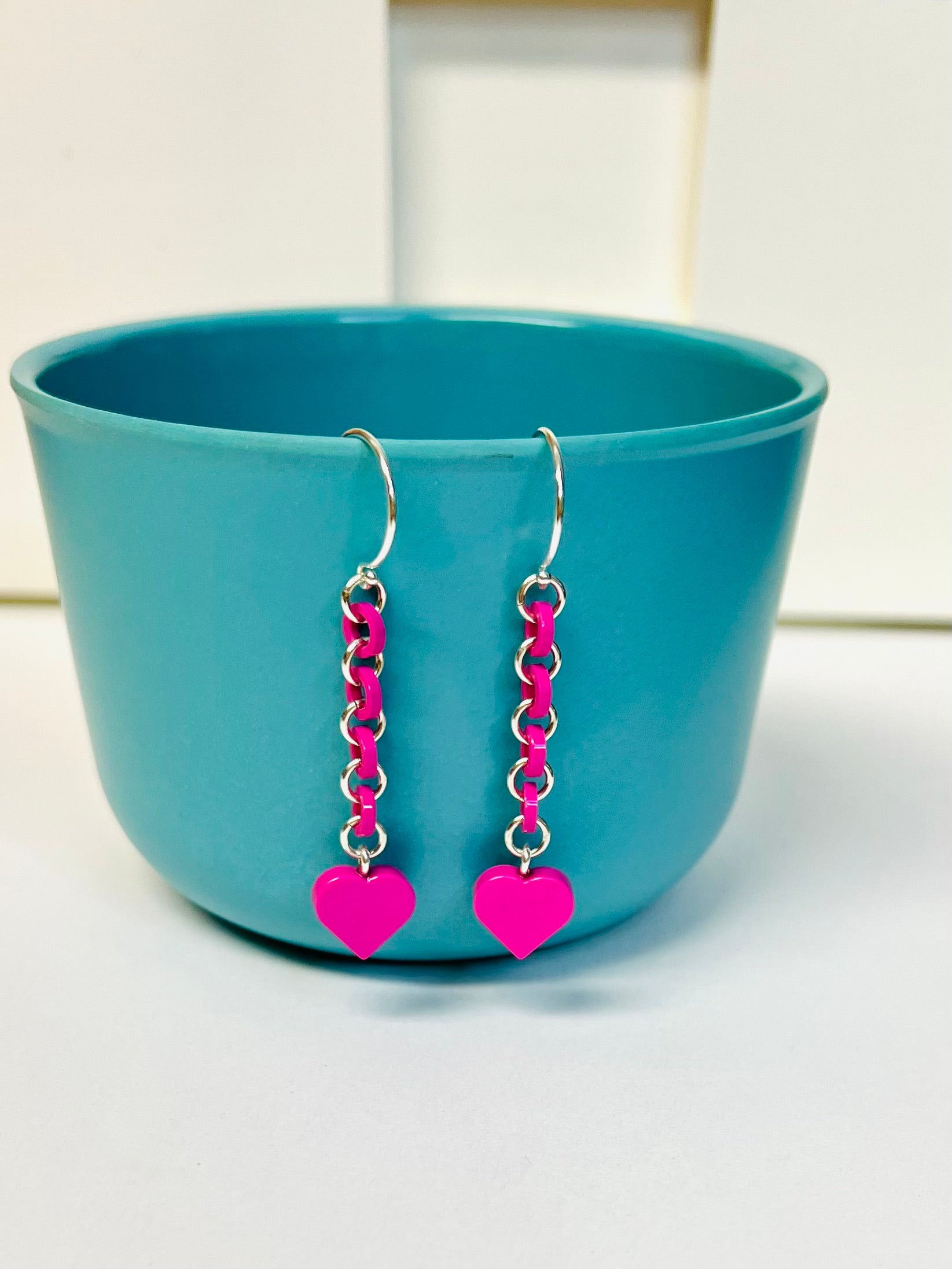 Earrings are displayed hanging off a cup. The earrings have silver jump rings alternating with loops made  from cutting off the top studs of pieces of LEGO bricks. LEGO dot heart dangles from the bottom