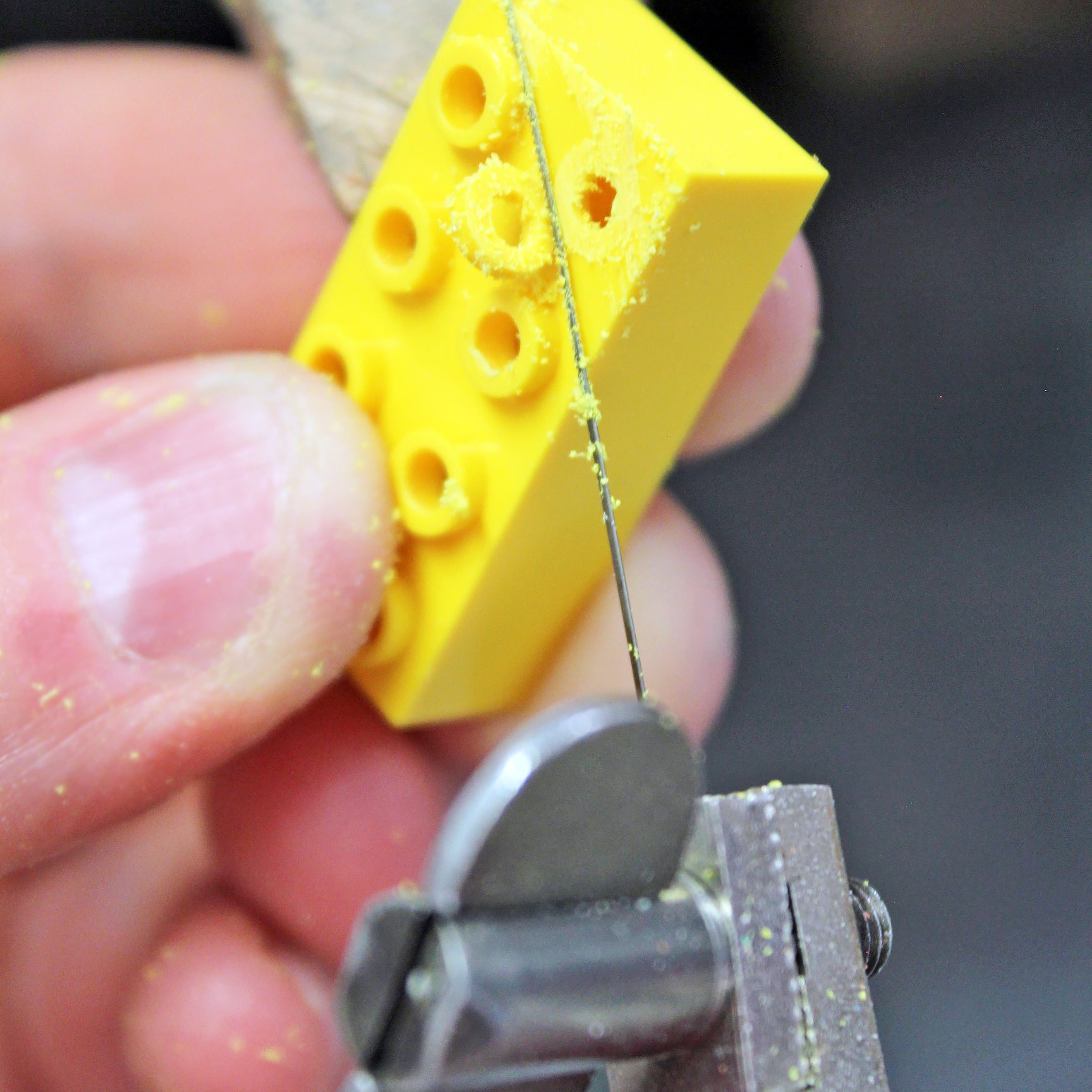 a yellow ego brick being held while hand sawing off the top pieces to demonstrate what the earrings are created from