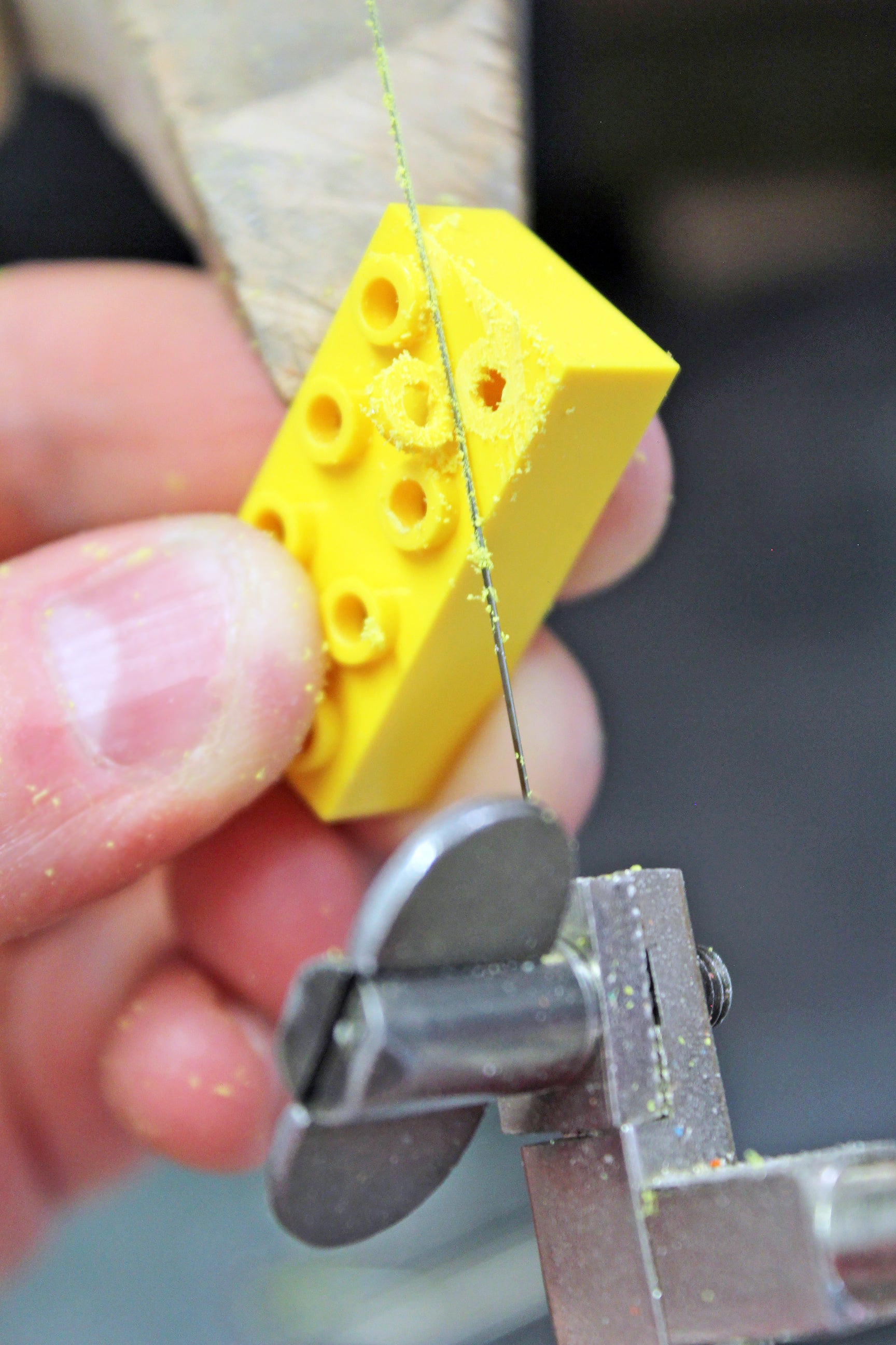 a yellow ego brick being held while hand sawing off the top pieces to demonstrate what the earrings are created from