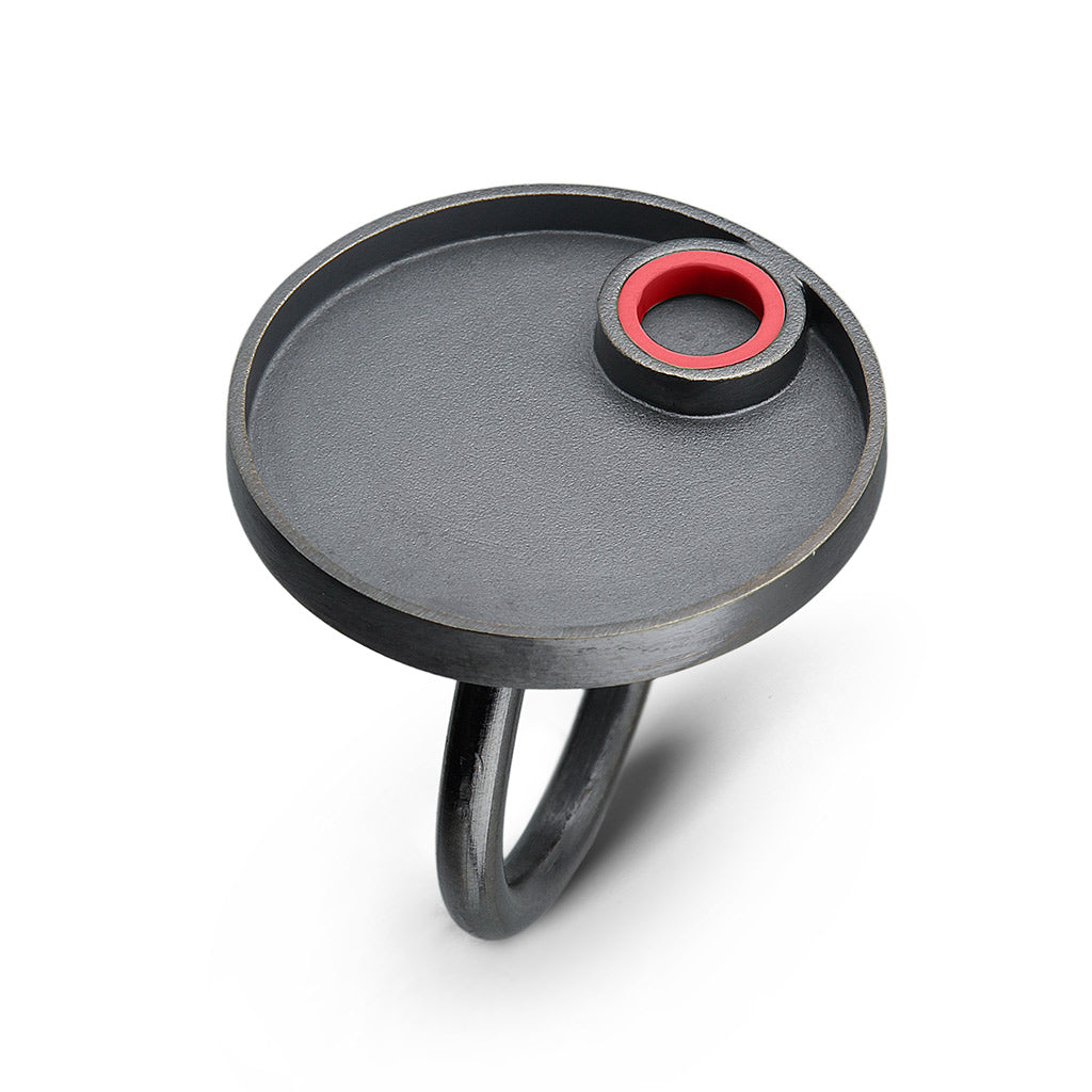 a sterling silver oxidized ring with a circle design on top with a red lego piece made into a tube on the top  surrounded by silver