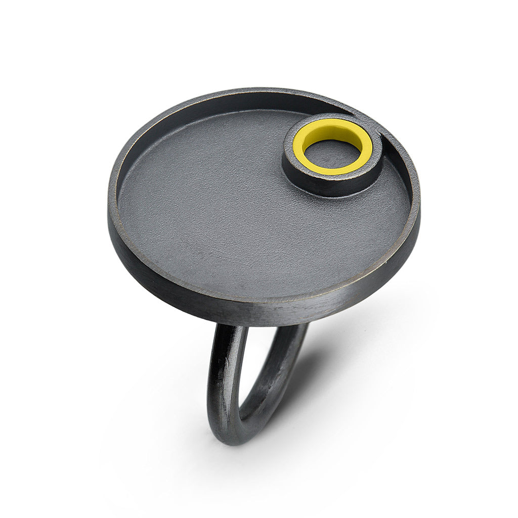 a sterling silver oxidized ring with a circle design on top with a yellow ego piece made into a tube on the top  surrounded by silver