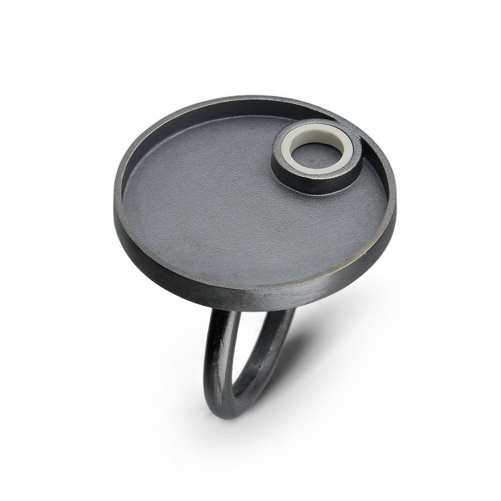 a sterling silver oxidized ring with a circle design on top with a white lego piece made into a tube on the top  surrounded by silver