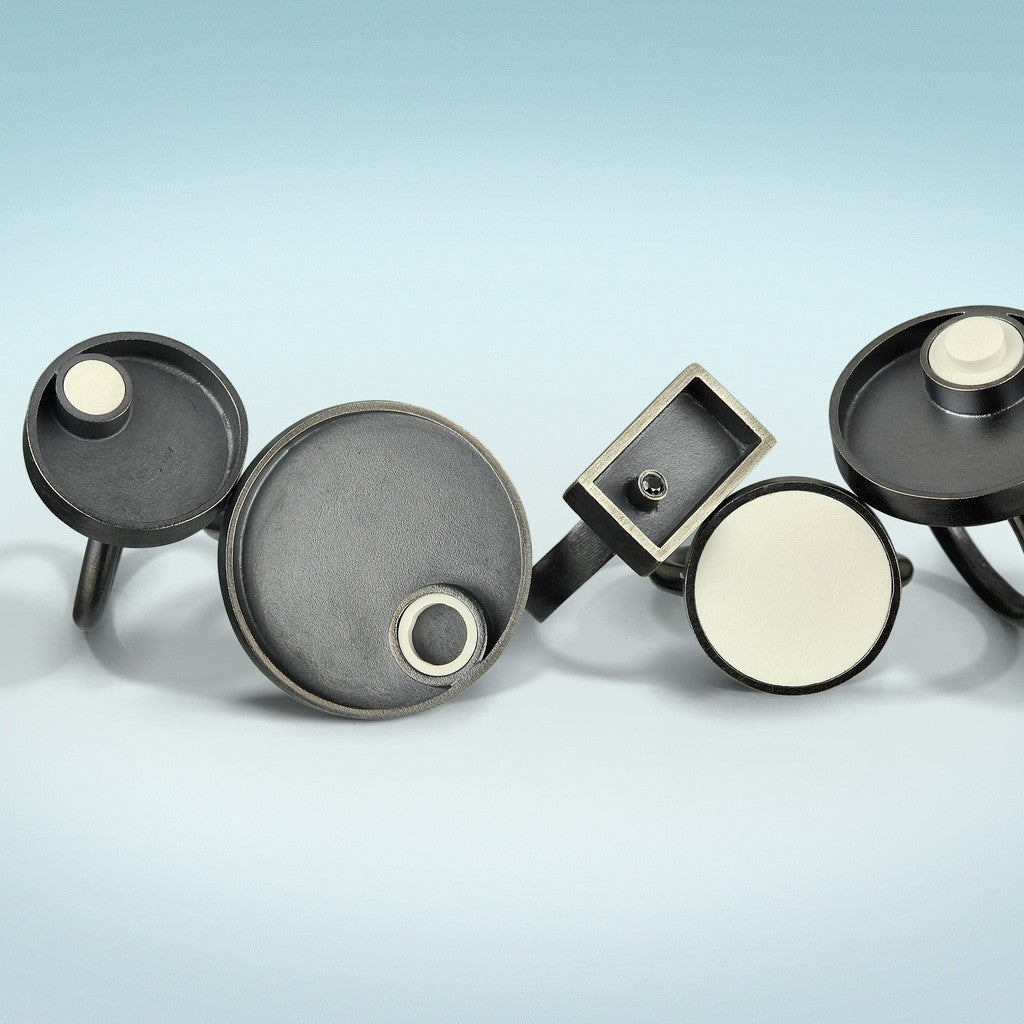 a group of 5 sterling silver rings with oxidized finish. 4 rings are circle design with recycle white lego  set into them. The other style is a rectangle with a black diamond set off center on to one side