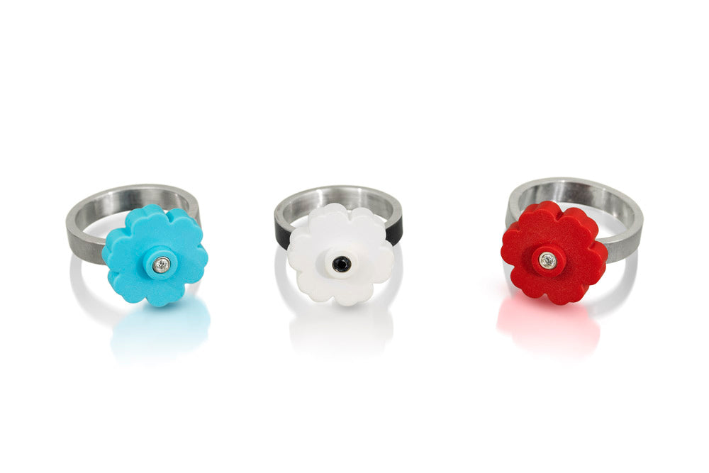 a photo of 3 LEGO flower rings, one is a turquoise flower  with a white diamond, one is a white flower with black diamond, last one is a red flower with a white diamond