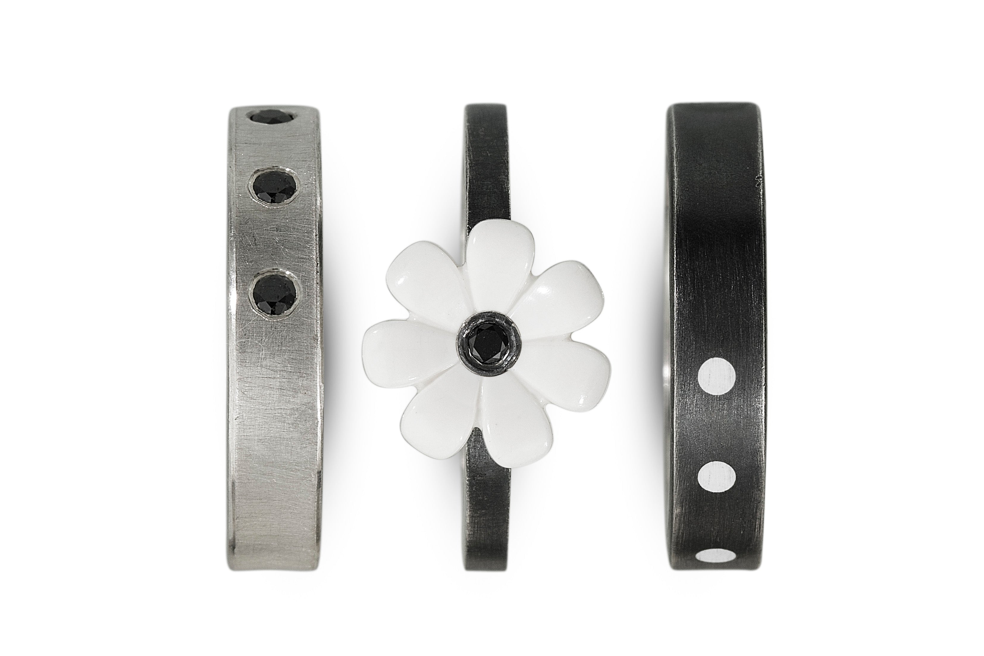 3 rings shown separate to show style. Middle ring has a white lego flower with a black diamond in the center. 2 bands on either side
