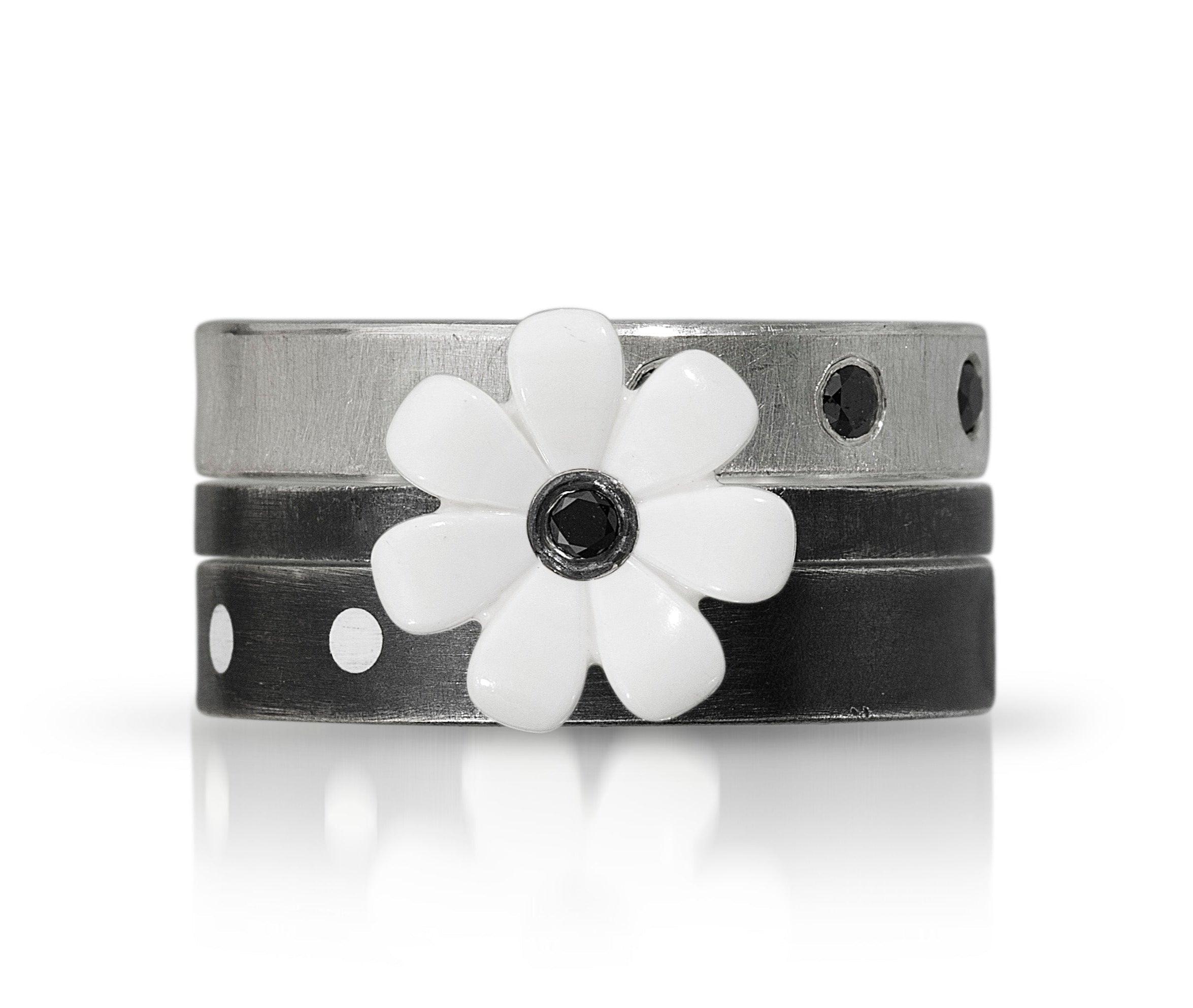 3 rings stacks on top of each other to show how it looks on finger. Top band has black diamonds set into sterling silver. middle ring is a white lego flower with a black diamond in the middle. last band has an oxidized finish with 2 white dots that are from recycled lego set into metal