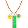 3 charms on a light brown leather cord-a yellow lego daisy with a green diamond in center, a 1 x 4 green lego brick set in silver, and a tan round lego dot with a small green dot in its center