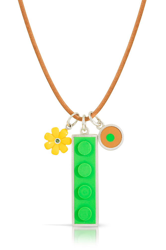 3 charms on a light brown leather cord-a yellow lego daisy with a green diamond in center, a 1 x 4 green lego brick set in silver, and a tan round lego dot with a small green dot in its center