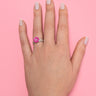 Hand wearing a pink lego daisy ring with a diamond in the center on a pink background