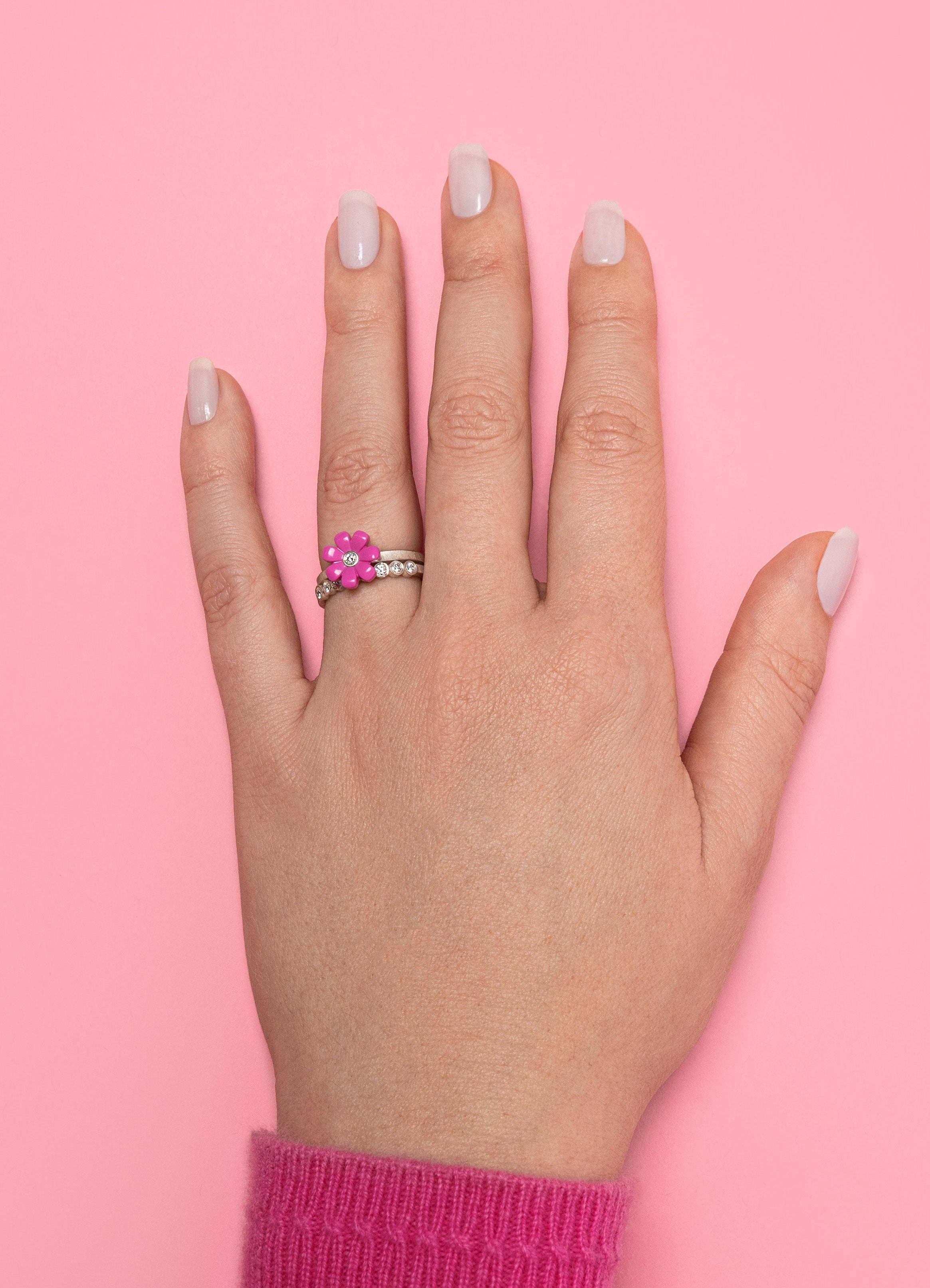 Hand wearing a pink lego daisy ring with a diamond in the center on a pink background