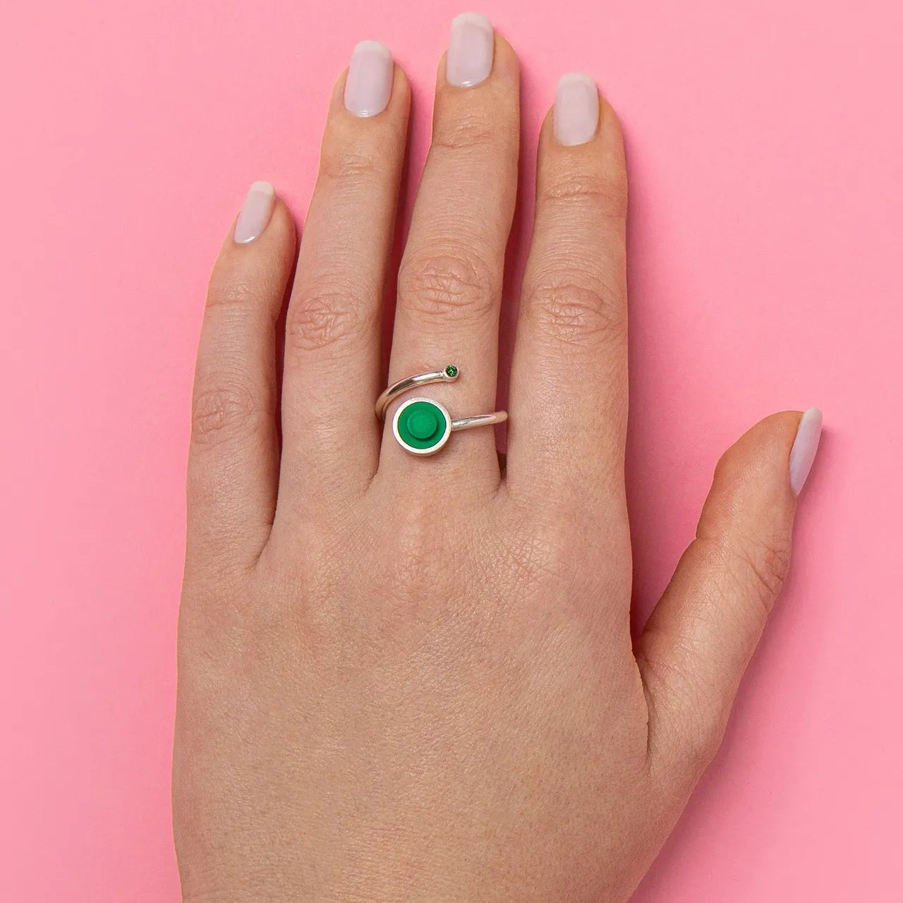 Hand wearing a green diamond ring  with a green lego stud on a pink background
