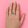 Hand wearing a green diamond ring  with a green lego stud on a pink background