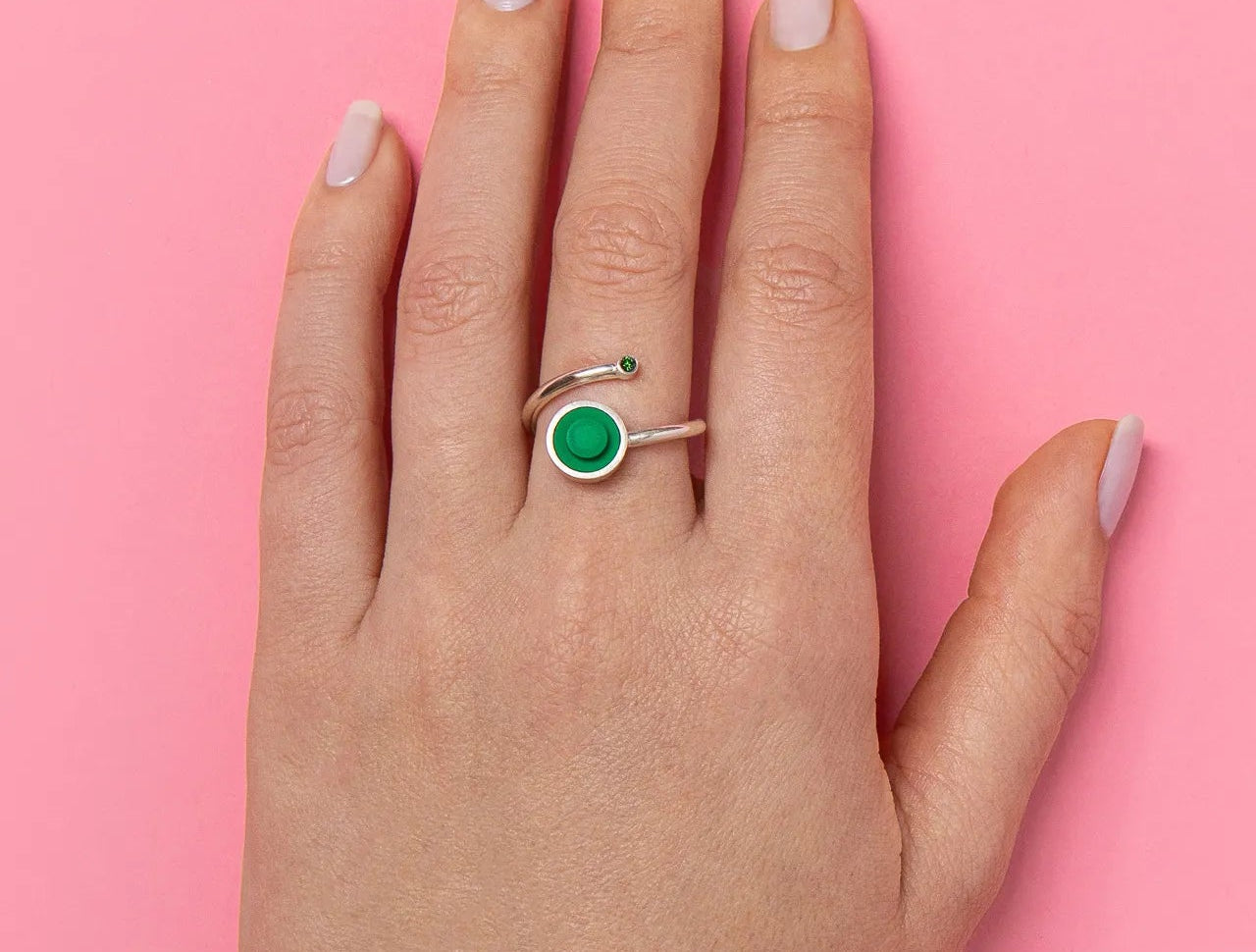 Hand wearing a green diamond ring  with a green lego stud on a pink background