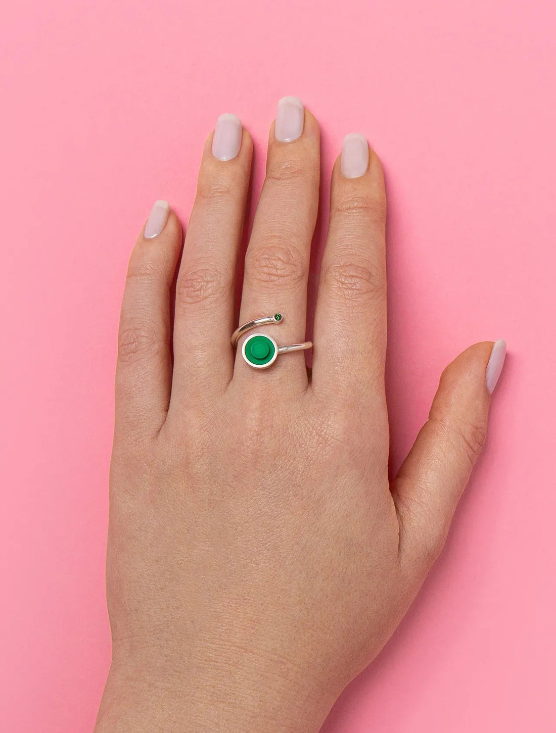 Hand wearing a green diamond ring  with a green lego stud on a pink background