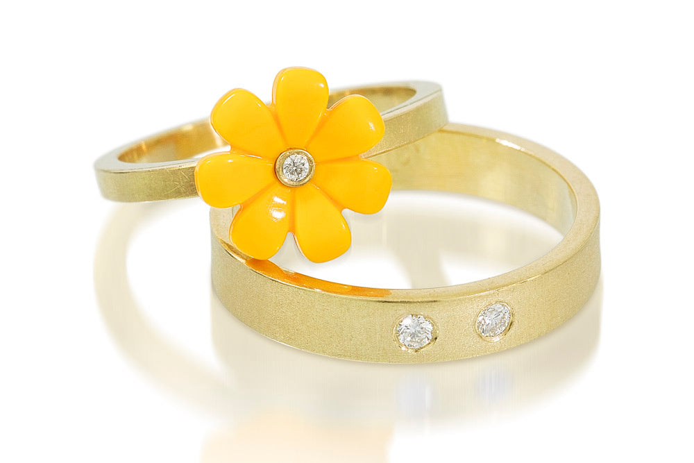 LEGO friends flower in yellow with a diamond set n the center on top of a gold ring leaning up against another ring that is a gold band with diamonds set into it
