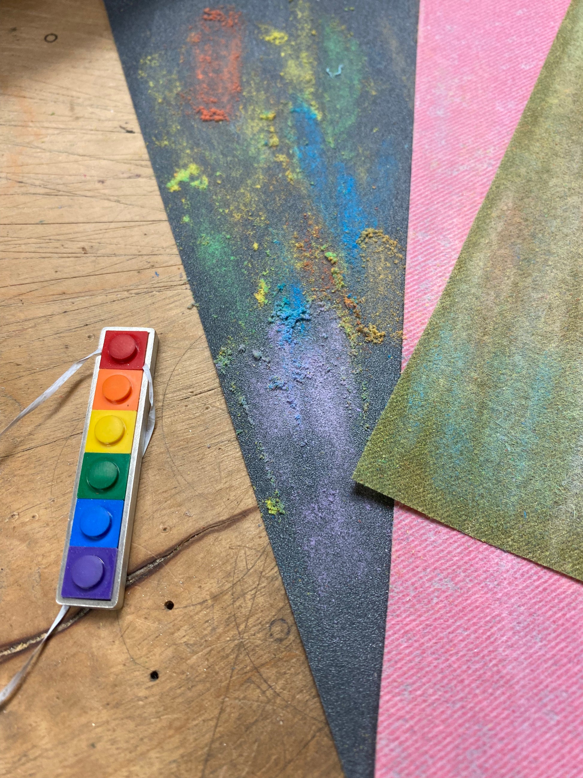 On the work bench showing the step of how the lego pieces are tested to fit tightly by putting them inside the bezel using dental floss underneath so they can be taken out with a pull on the dental floss. Sandpaper is shown in different grids with lego dust on them to show how the lego are sanded 