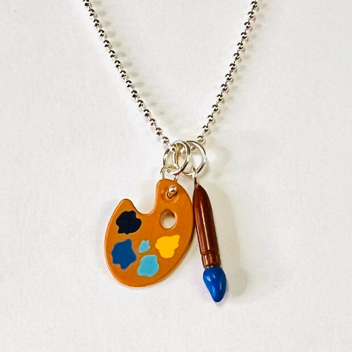 Lego palette and paint brush toy charms hanging of a sterling silver chain. Palette has light blue, dark blue , yellow and black paint like palette Vincent would have used for his Starry Night Master piece painting 