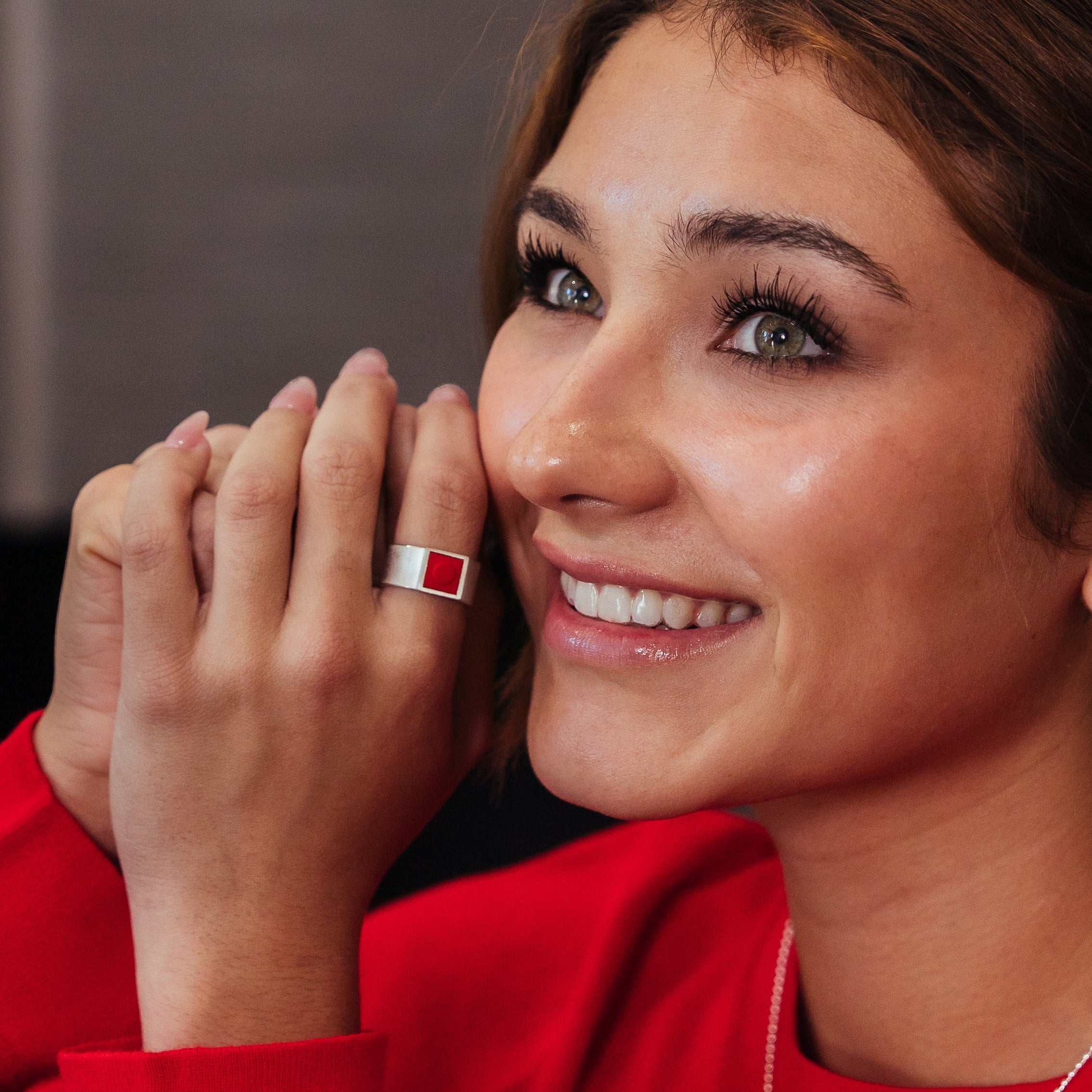 Woman wearing red jewelry including a ring and earrings, with a blurred background.