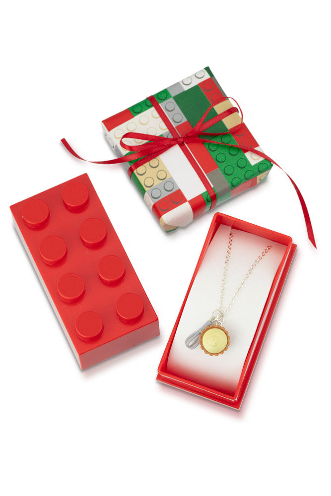 Red Lego gift box wrapped in Lego pattern paper with red bow, displayed with a Lego charm necklace inside.
