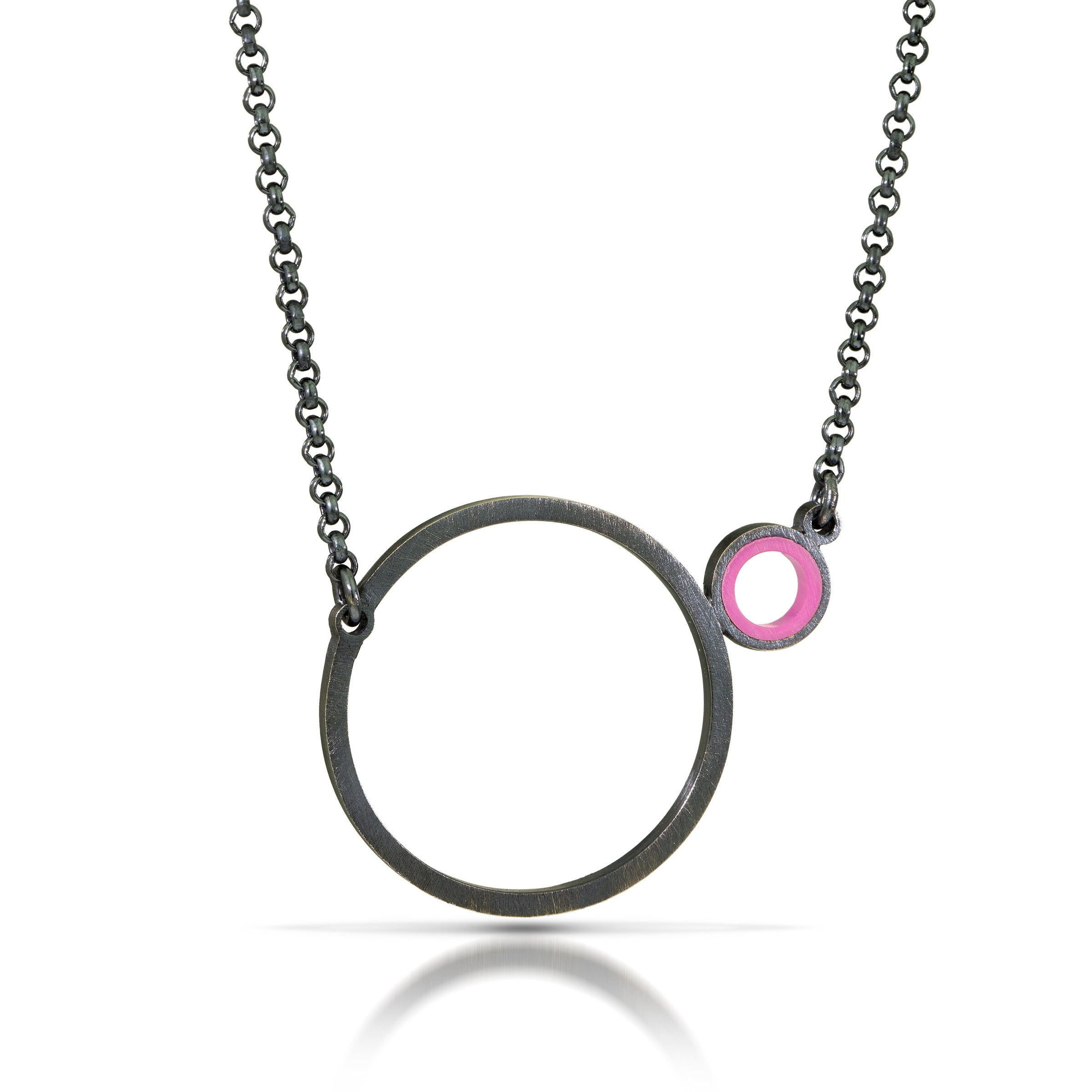 a necklace with a dark finish on the metal with a large circle pedant in center with a small circle attached to the side with a dark pink recycled piece of a lego tube inside the small circle