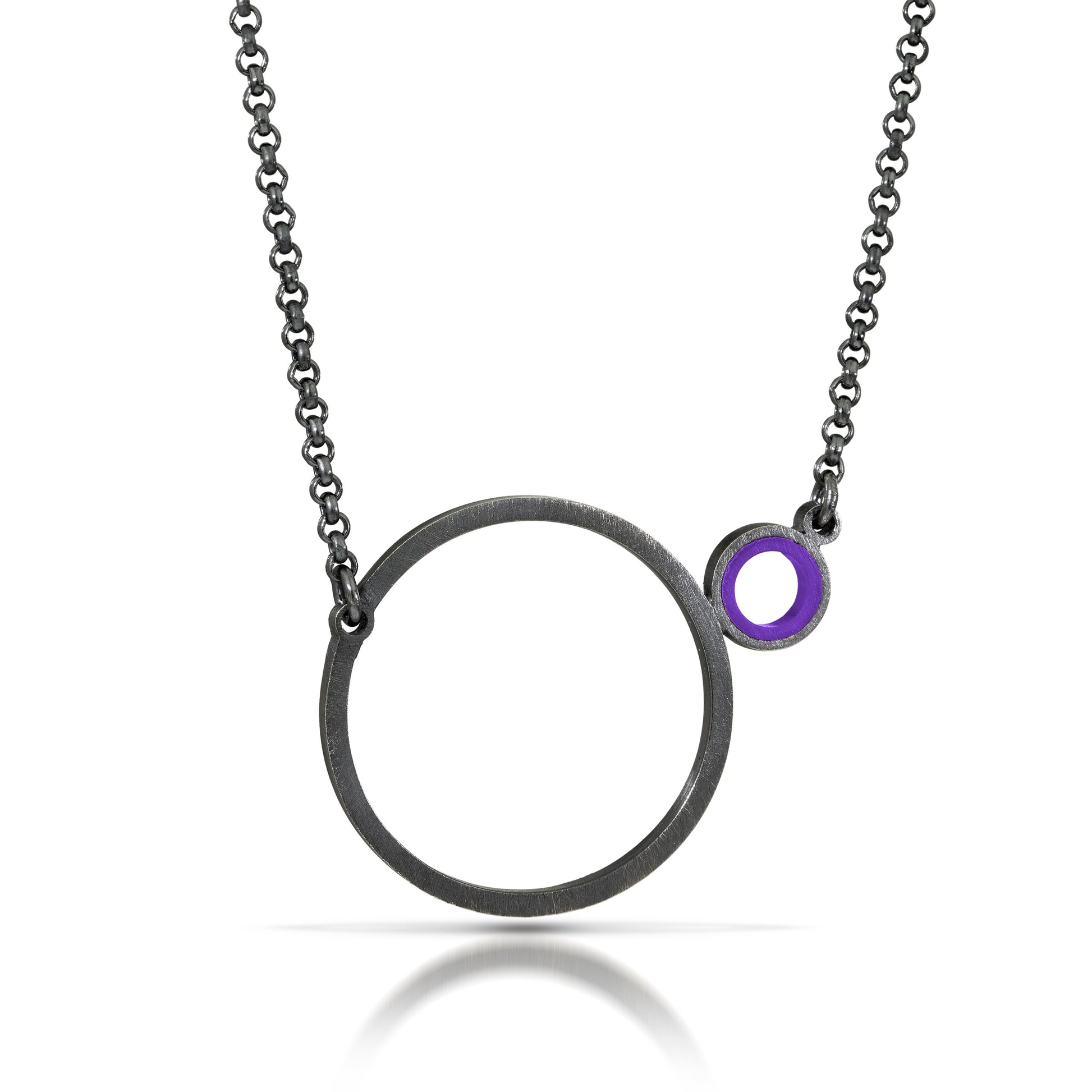 a necklace with a dark finish on the metal with a large circle pedant in center with a small circle attached to the side with a purple recycled piece of a lego tube inside the small circle