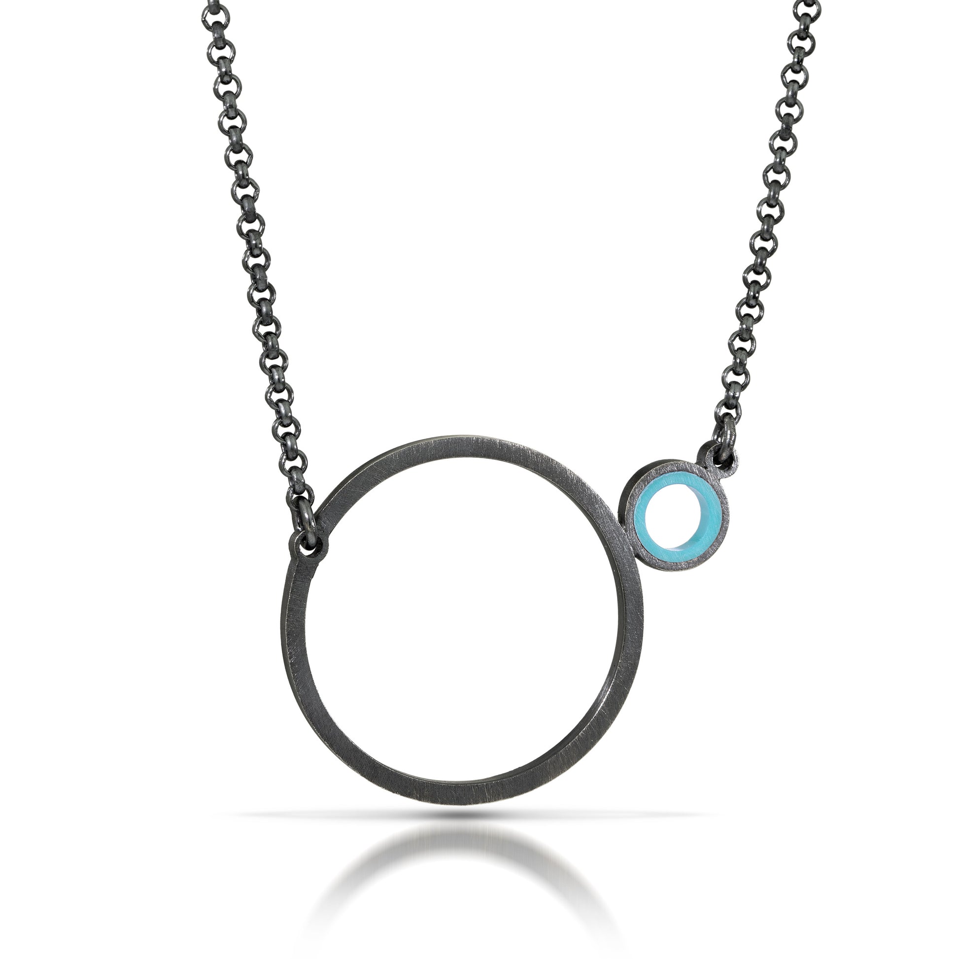 a necklace with a dark finish on the metal with a large circle pedant in center with a small circle attached to the side with a turquoise recycled piece of a lego tube inside the small circle