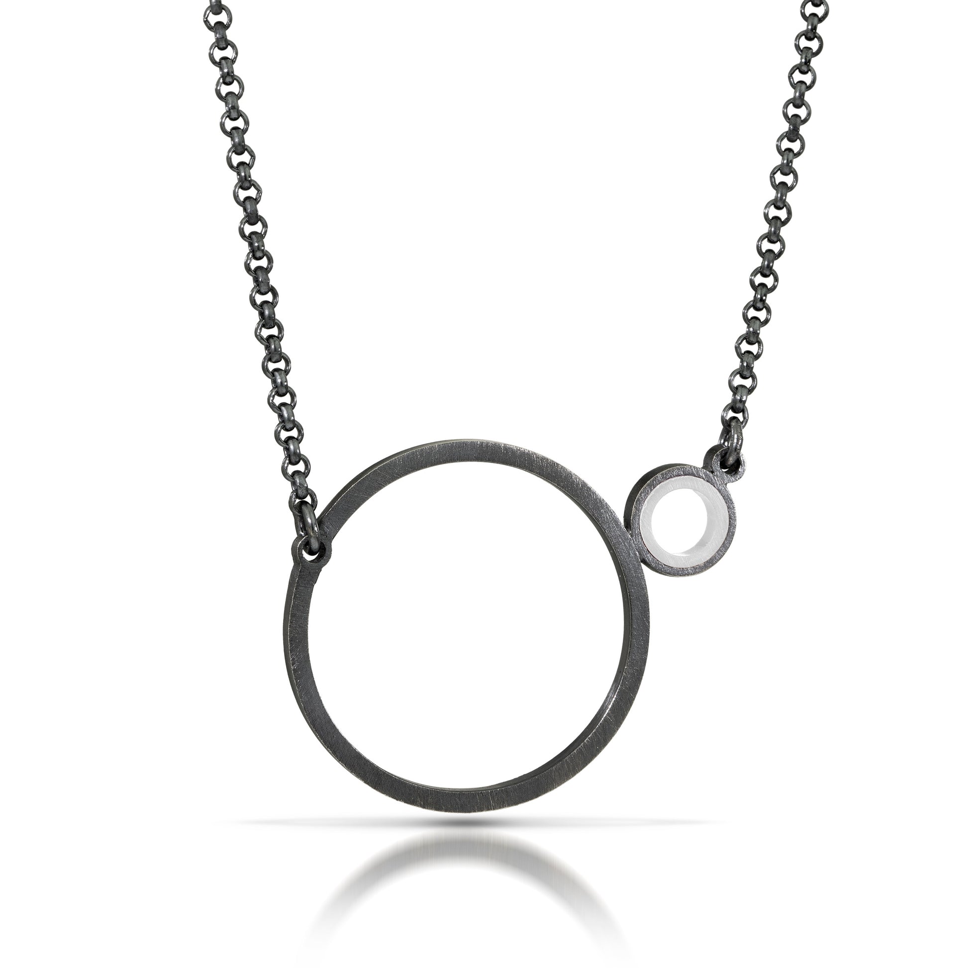 a necklace with a dark finish on the metal with a large circle pedant in center with a small circle attached to the side with a white recycled piece of a lego tube inside the small circle