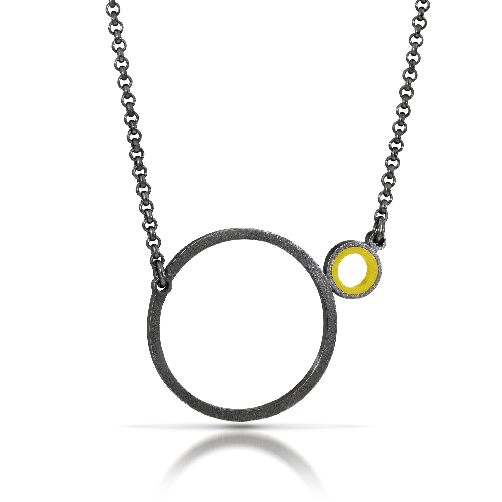 a necklace with a dark finish on the metal with a large circle pedant in center with a small circle attached to the side with a yellow recycled piece of a lego tube inside the small circle