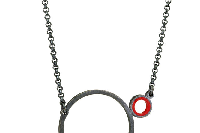 a necklace with a small circle with red inside on the side of a larger circle 