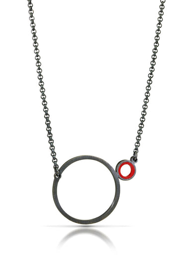 a necklace with a dark finish on the metal with a large circle pedant in center with a small circle attached to the side with a red recycled piece of a lego tube inside the small circle