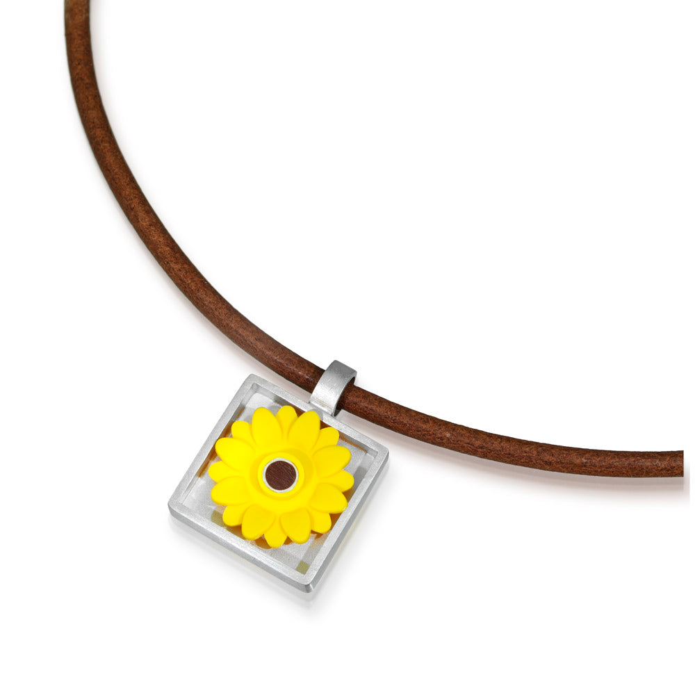 plasic yellow sunflower with a brown center in a silver frame as a pendant on a brown leather cord 