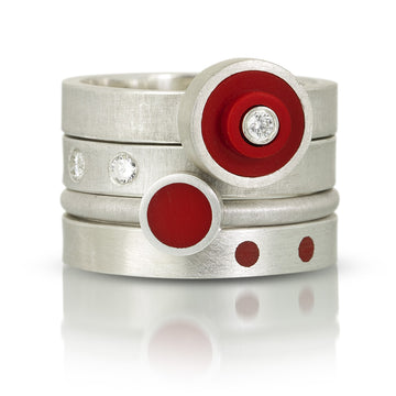 4 lego rings stacked on top of each other. First one is a round red lego dot ring with a diamond in center. Udernated that one is a band with 2 diamonds set flush into ring. Next stacking ring is a recycled red lego circle stud piece set in silver. last one on the bottom is a silve band with 2 red dots on a silver band 