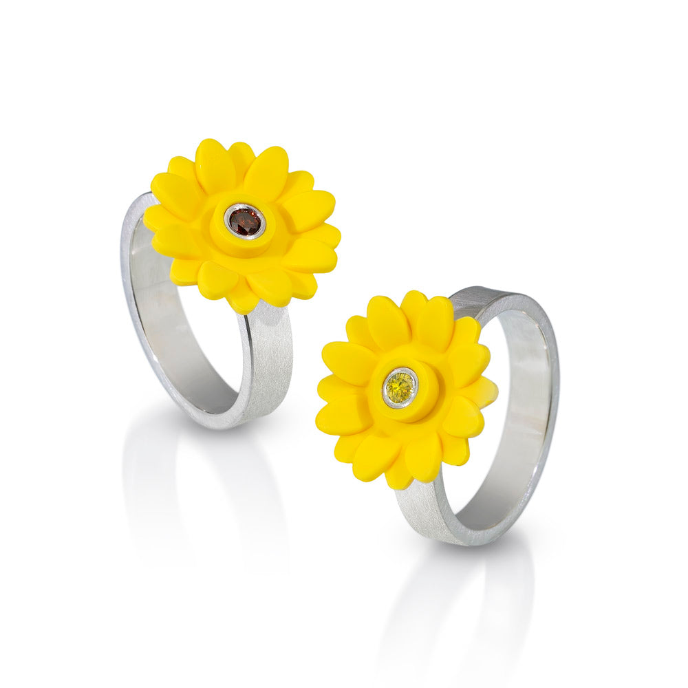 2 rings shown with yellow sunflowers on top of a flat silver band with colored diamonds set in the middle of the sunflower.