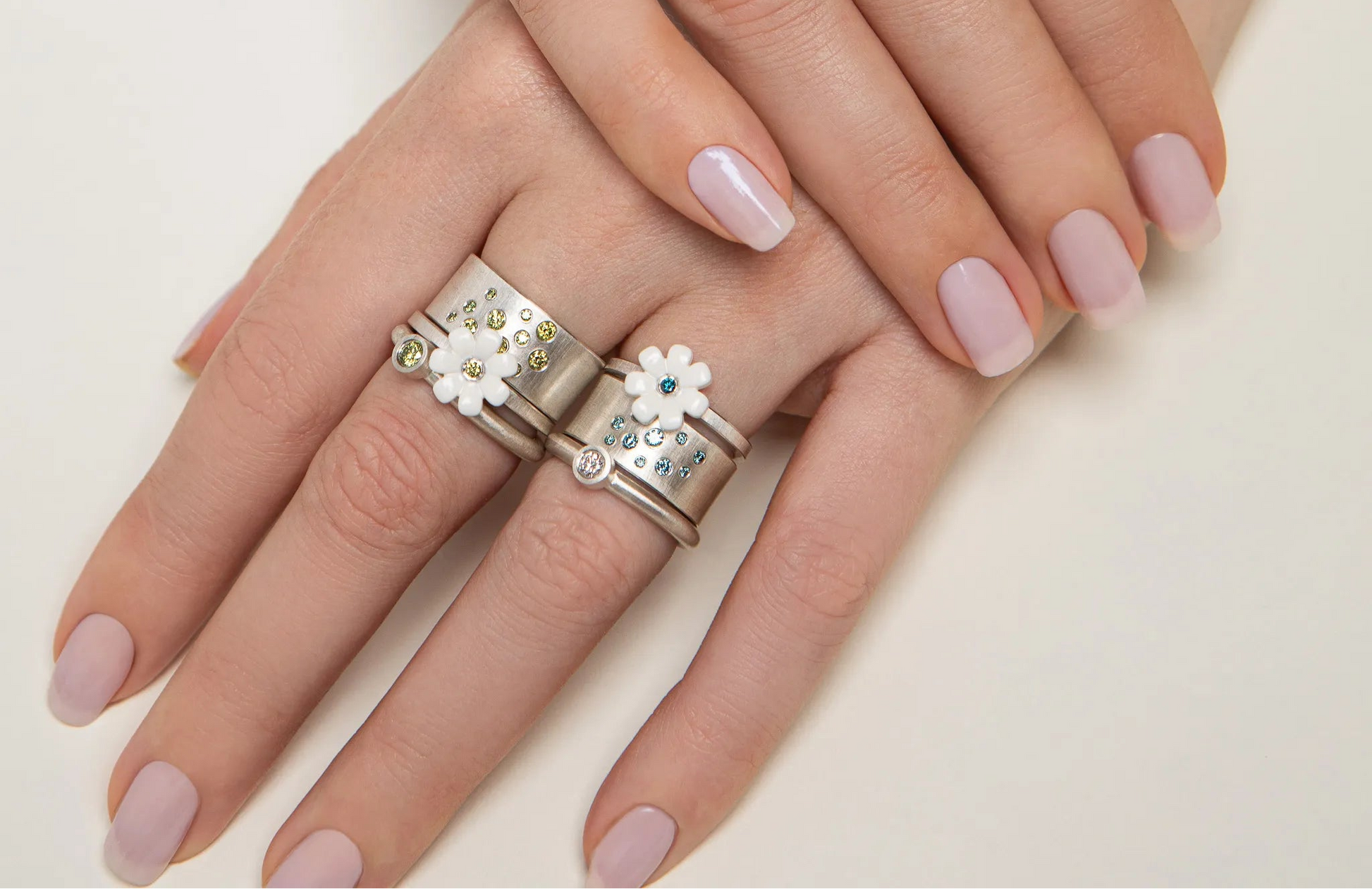 Close-up of a hand wearing two decorative rings with floral designs on a light background