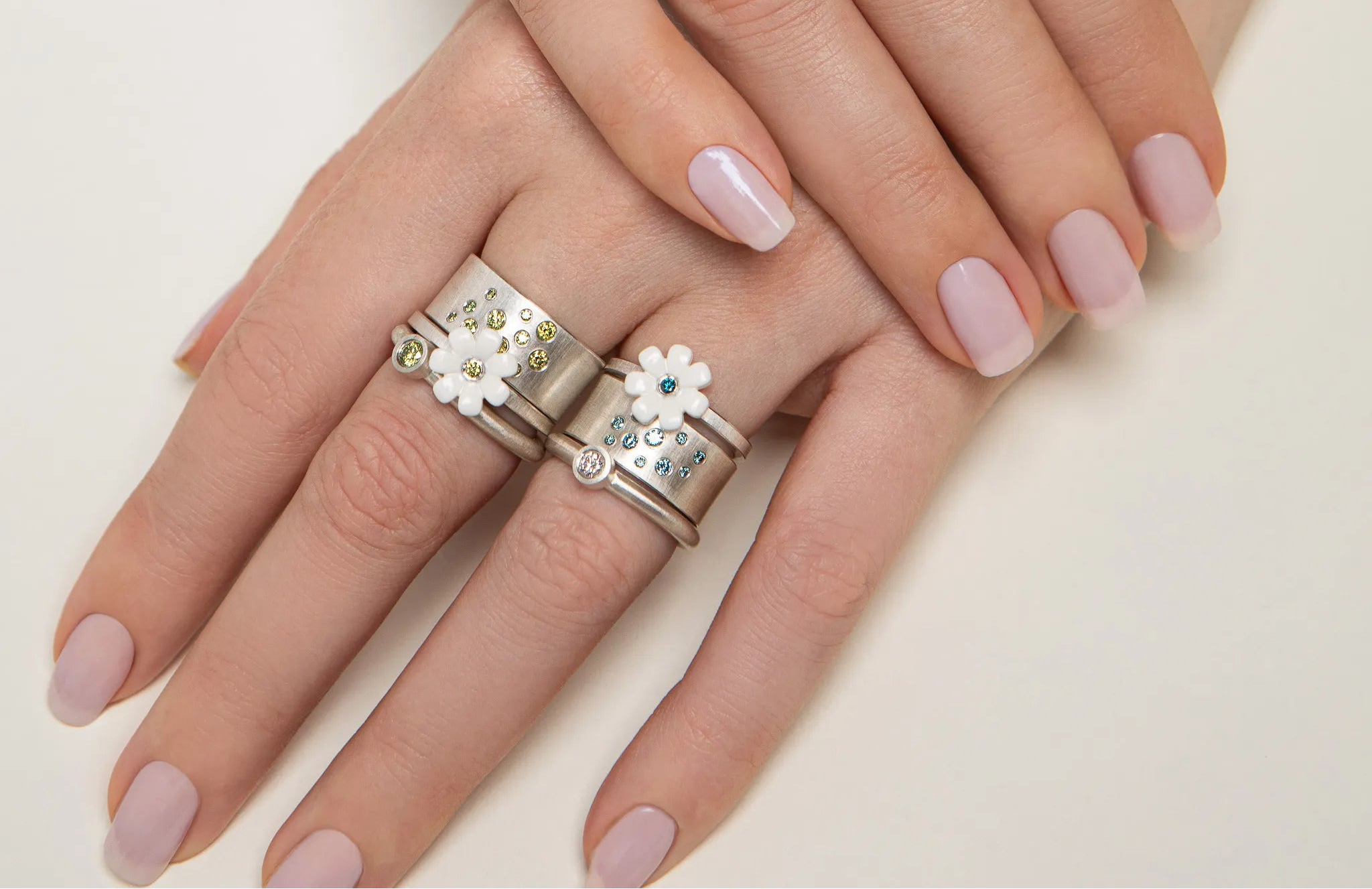 Close-up of a hand wearing two decorative rings with floral designs on a light background