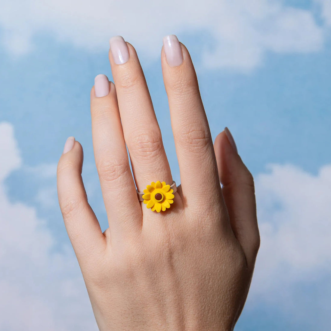 Hand wearing a yellow flower ring with a blue sky background